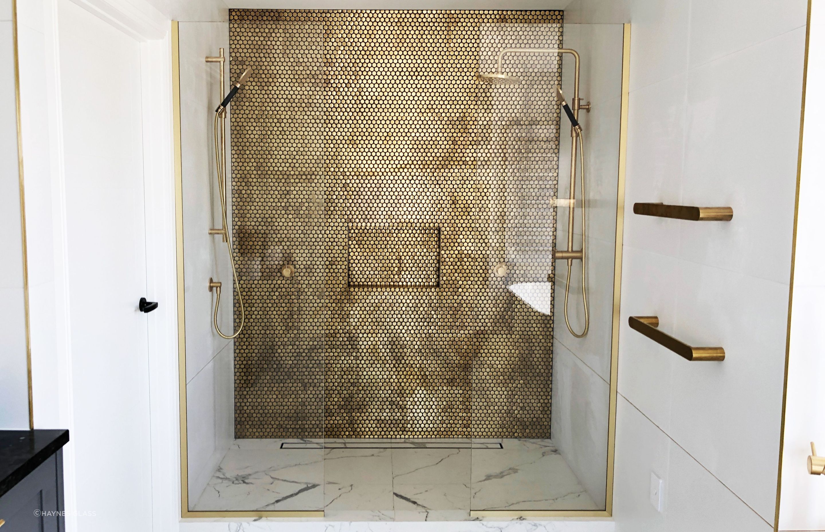 This fixed panel shower glass features gold hardware to match other gold fixtures in the bathroom.