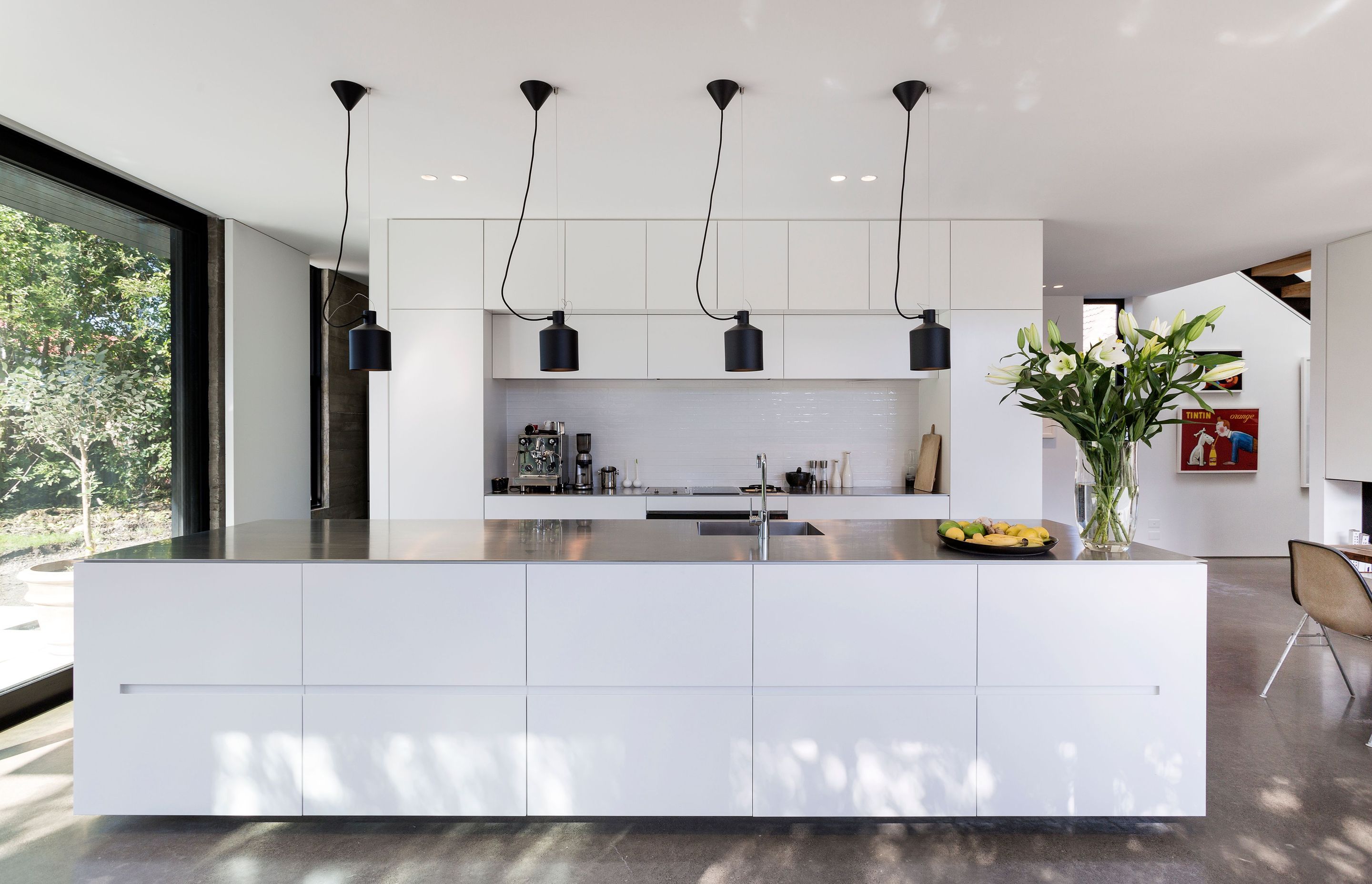 The monochromatic interior colour scheme includes an all-white kitchen with stainless steel benchtops and black lights and fixtures. 