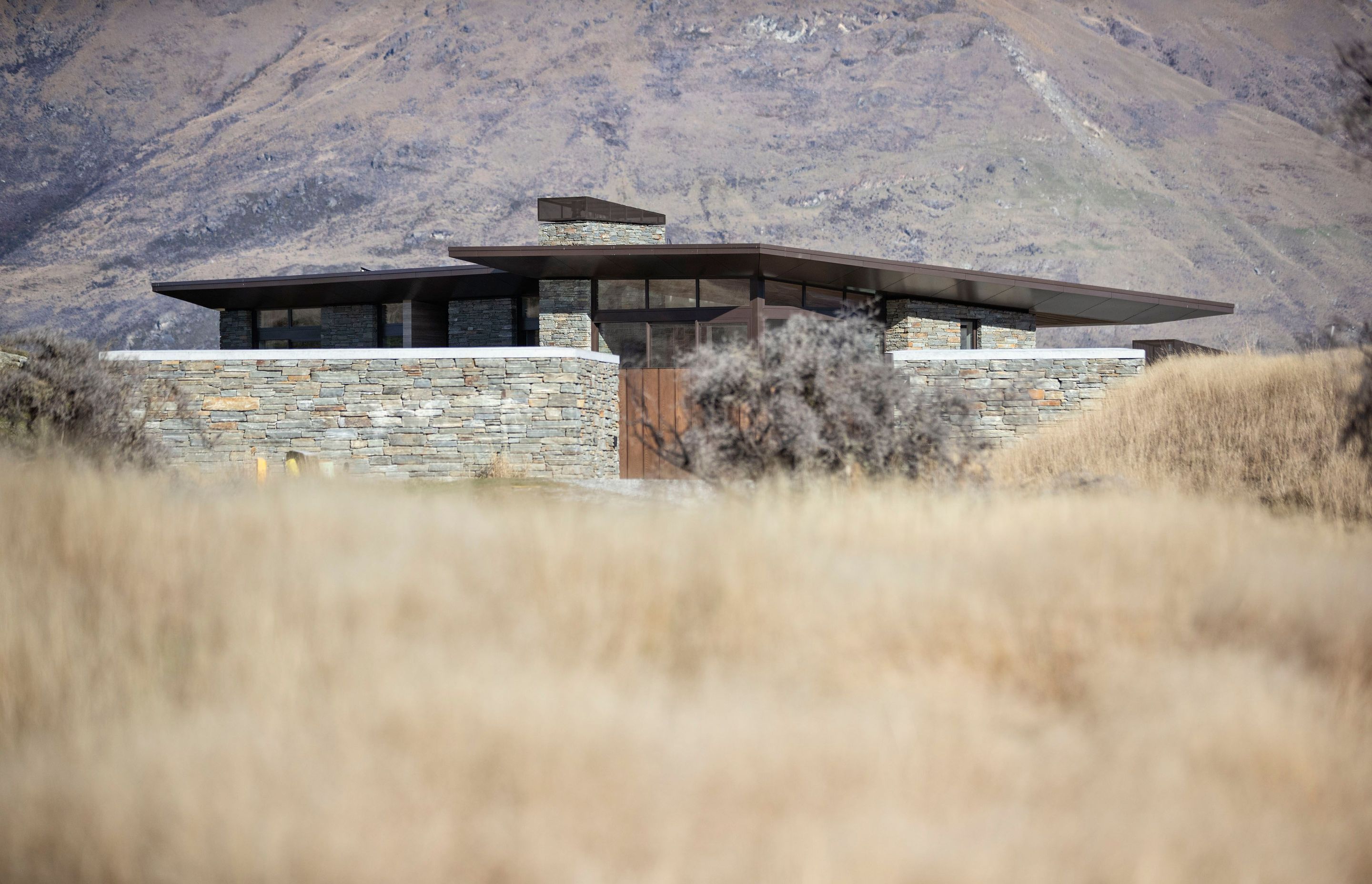 A low form, bronze aluminum joinery, cedar cladding and local schist help to blend the house into the surrounding tussock grasslands and rocky outcrops on the 1.272-hectare site. SD