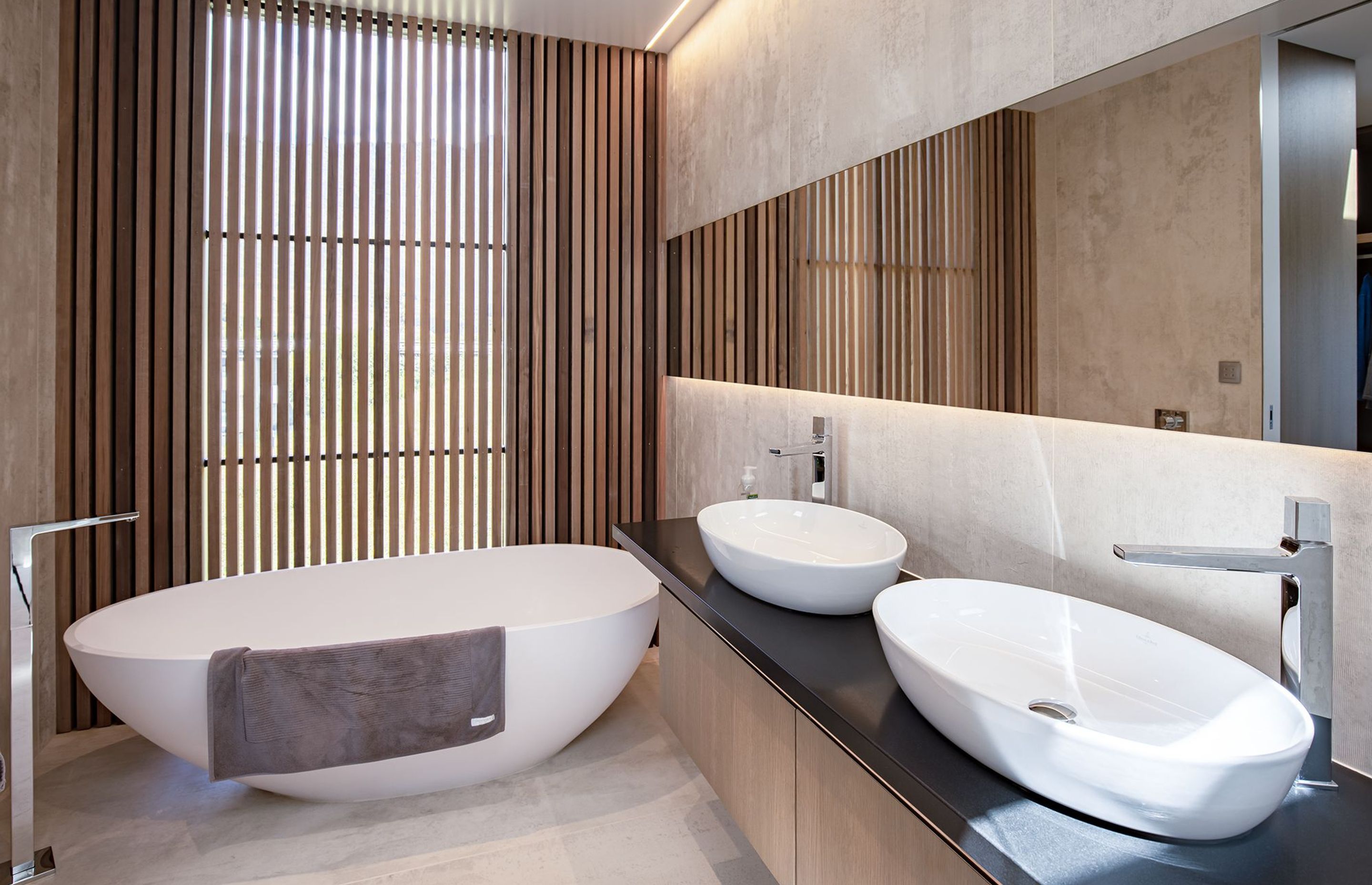 A curvaceous bath and sinks add another dimension to the sharp lines of the large-format tiling and the cedar screen.