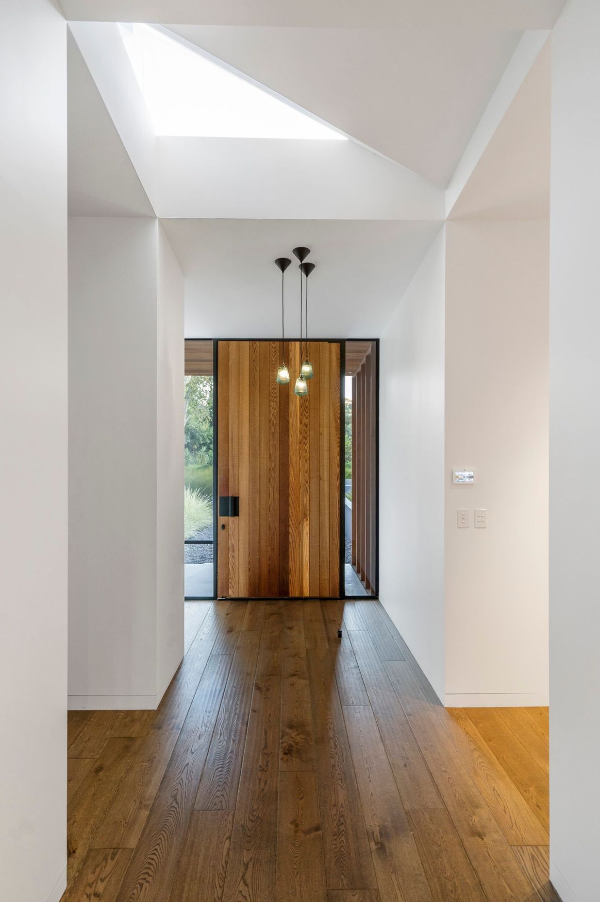  A cedar front door and dark oak flooring are top-lit by a triangular skylight.