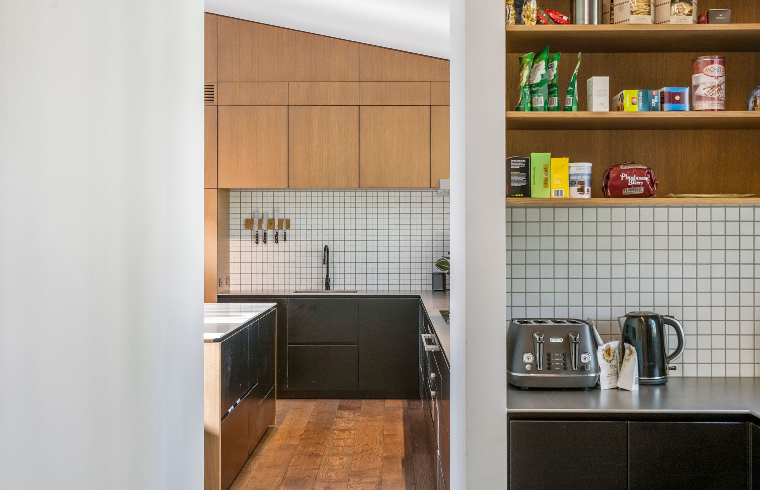 The adjacent scullery is hidden from the main kitchen and living area but is only a few paces away. White tiling with black grout and satin-finished steel worktops contrast the black and timber cabinetry.