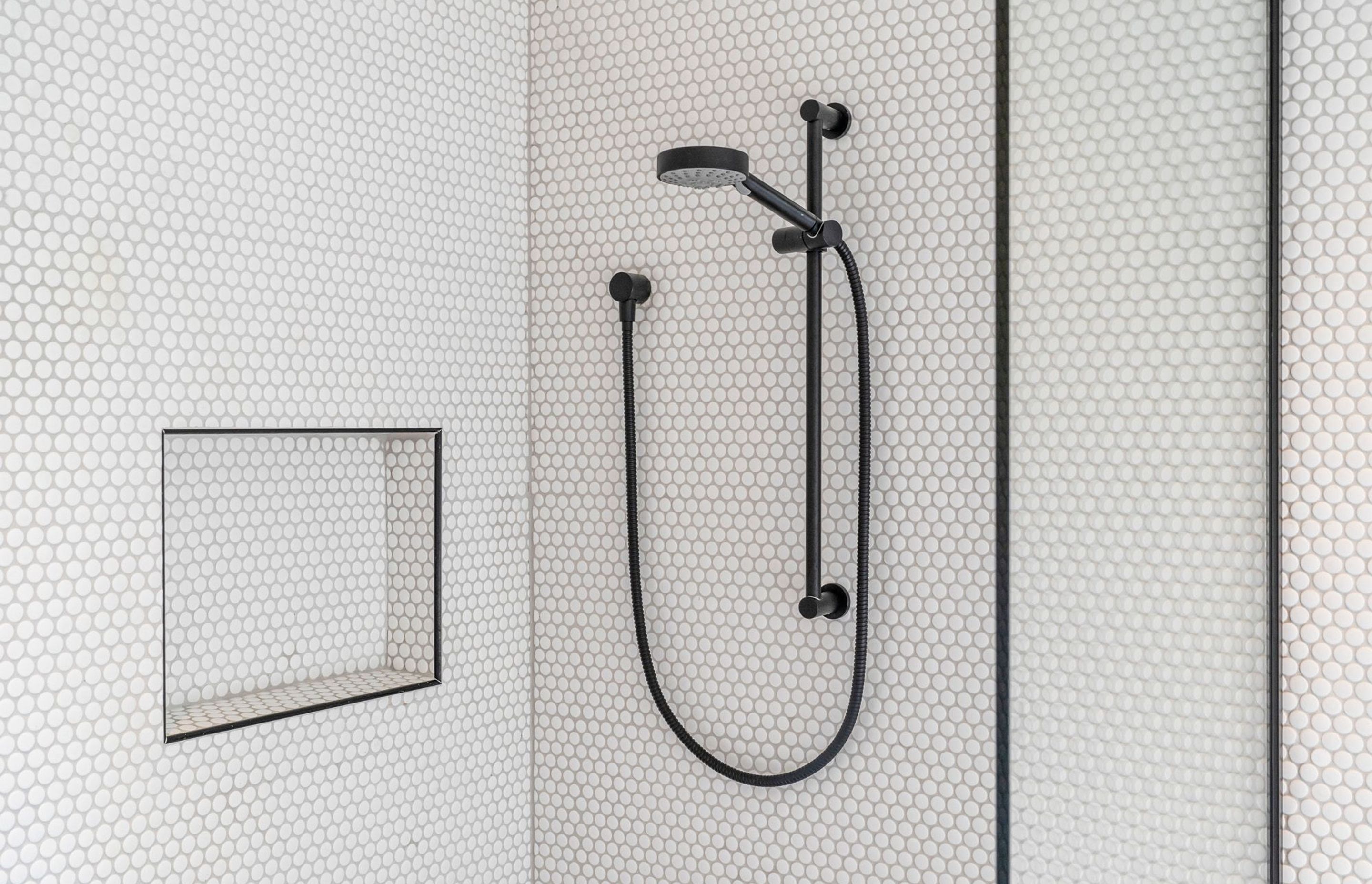 This monochromatic shower in the family bathroom contrasts modern black tapware against the small circular tiles.