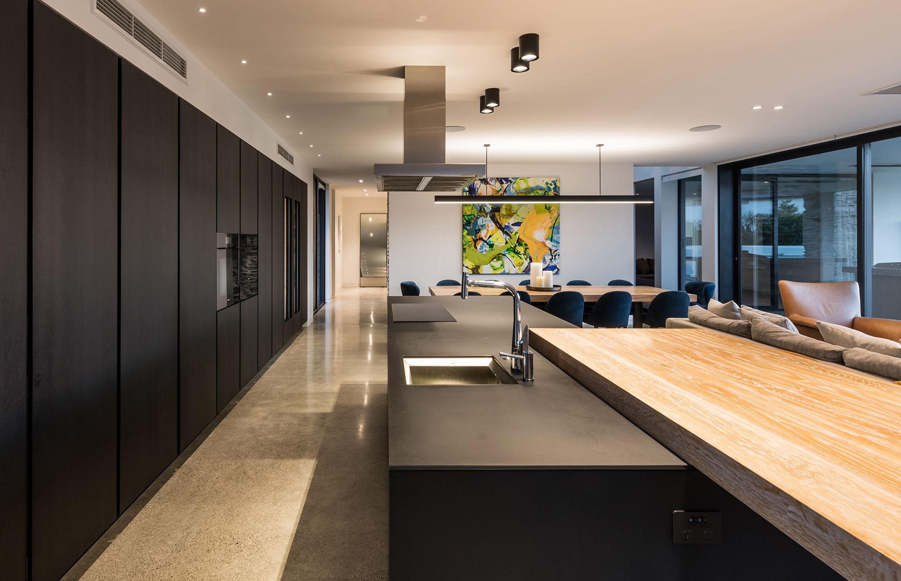 The Poliform kitchen features an expansive wall of cabinetry with built-in wine fridges and a long black island with a chunky timber breakfast bar.