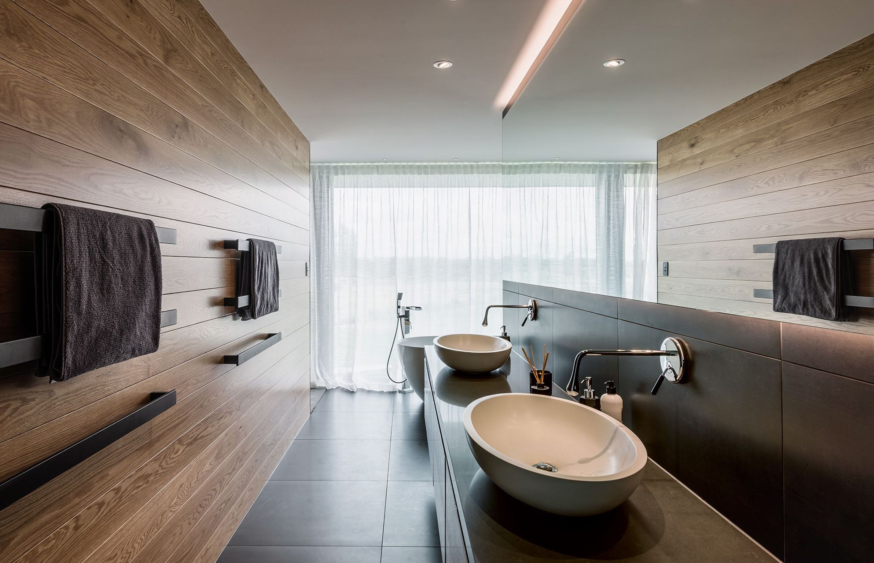 The en-suite bathroom is clad in horizontal timber paneling and large-format tiles