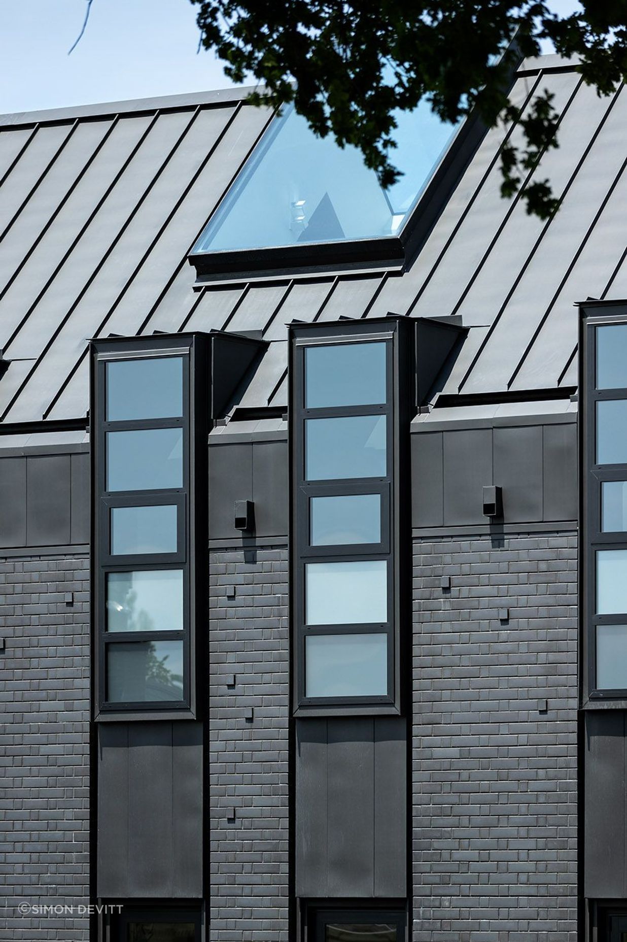 The northern facade is punctuated by a series of steel-lined dormer windows framing glimpses of borrowed landscapes from the neighbouring properties.