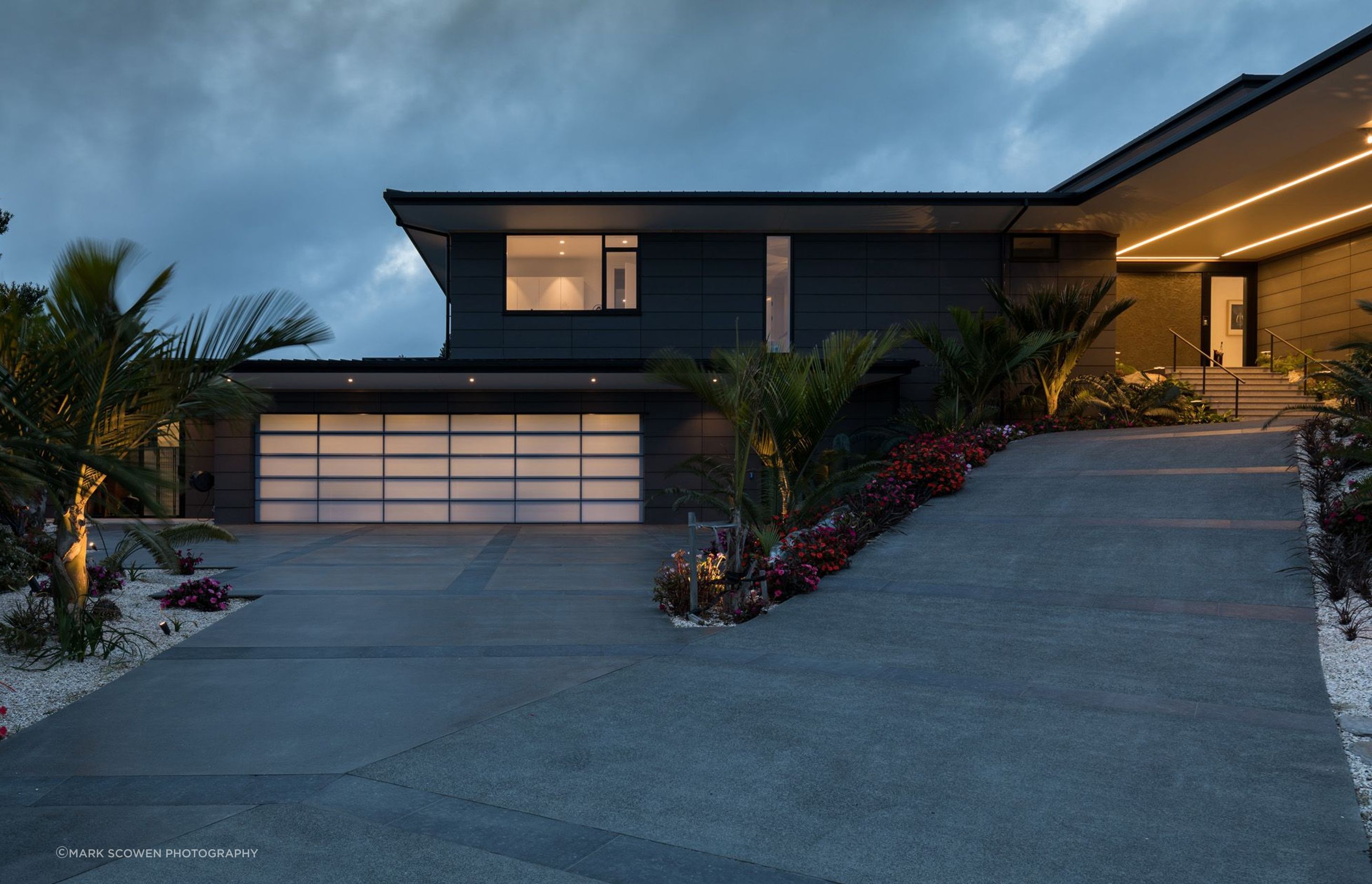 The front driveway leading the house is lined with sub-tropical plants. The garage (leftt) lights up like a lantern at night, while LED lights in the soffit direct visitors to the main entrance.