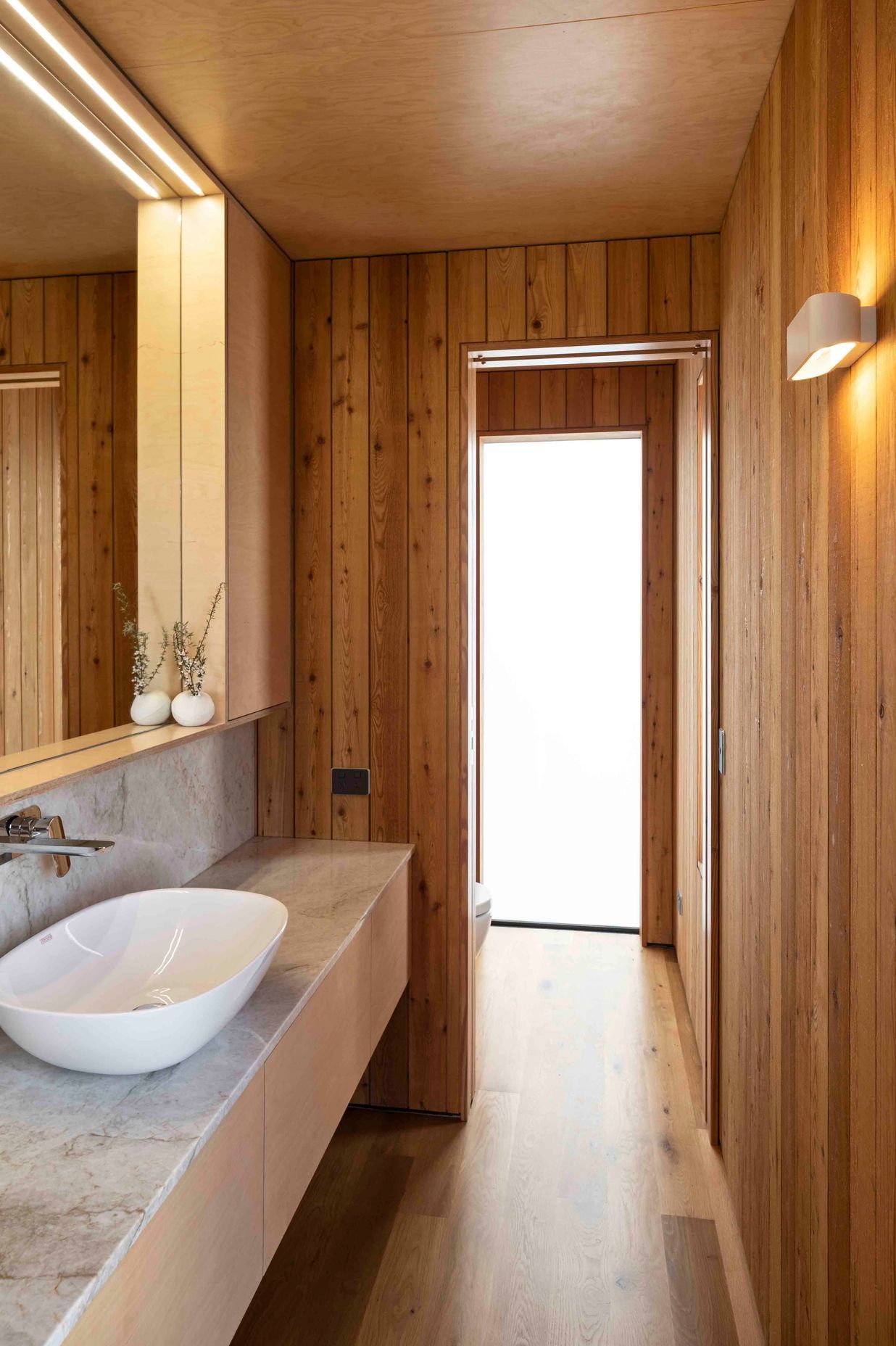 The bathroom's materiality ties easily into the biophilic theme of the house with Siberian larch walls, birch plywood ceilings and stone countertop.