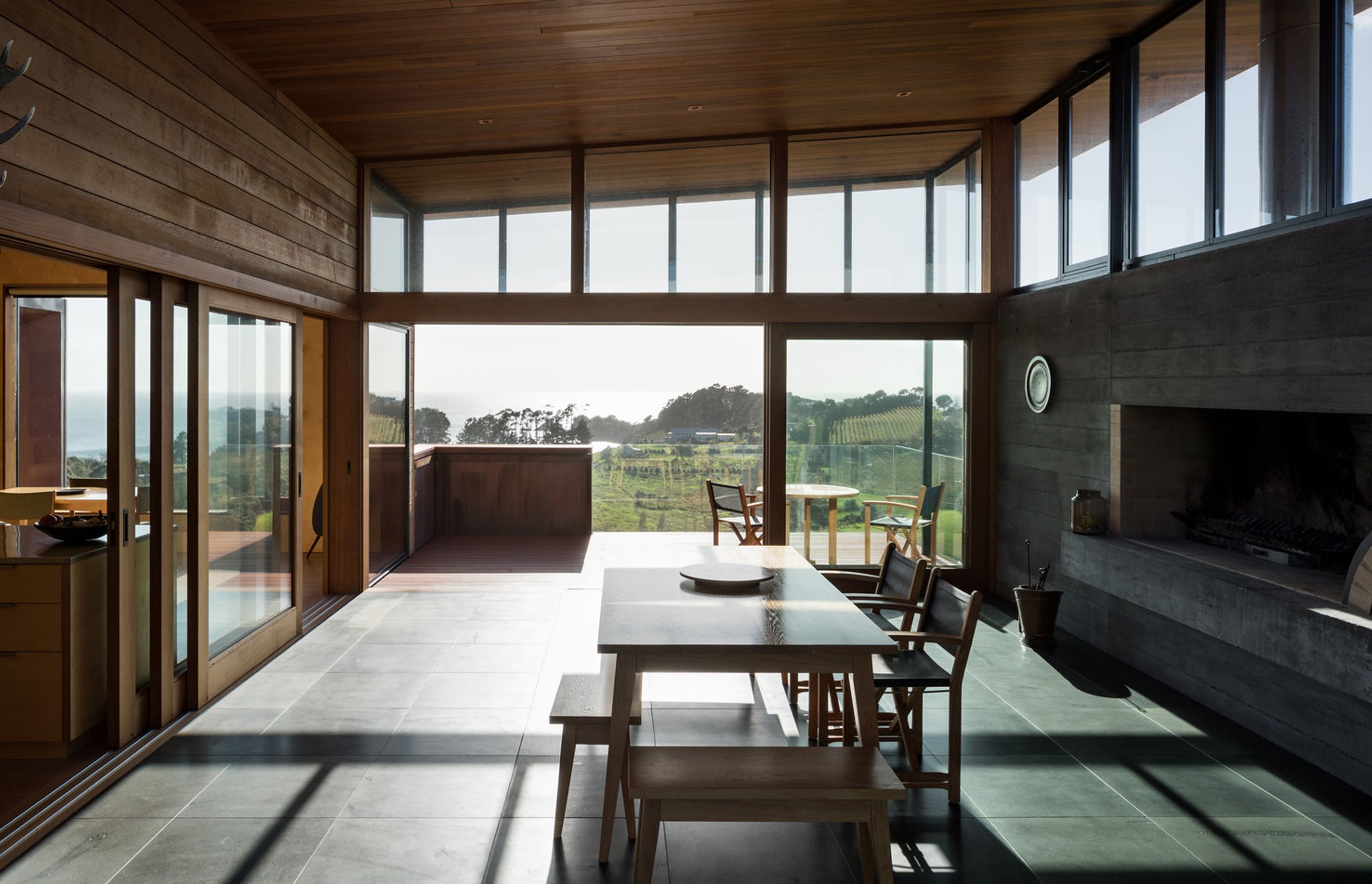 Looking through the entertainment room, across the balcony to expansive views over a vineyard of Syrah grapes, Oneroa Bay to the right and bush to the east.