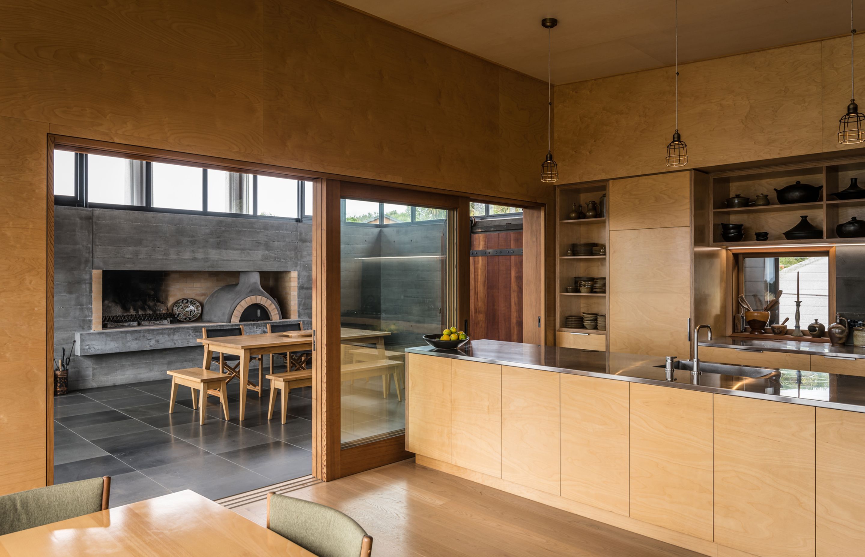 The bespoke plywood kitchen is a smooth and elegant contrast to the textured concrete and tiled floor seen in the entertainment room. Photograph by ArchiPro.