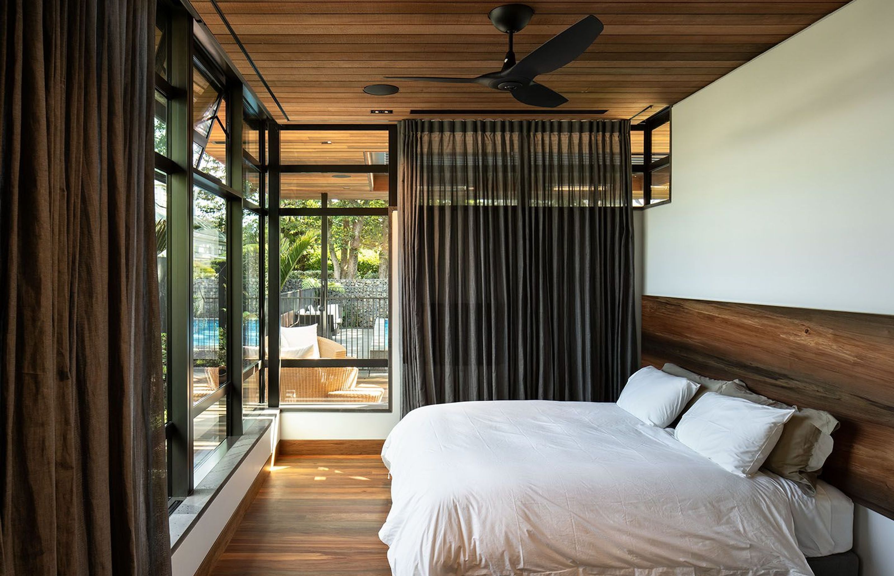 The bedroom looks out to the outdoor pool and a BBQ and seating area. The totara timber ceiling continues outside into the soffit of the exterior.