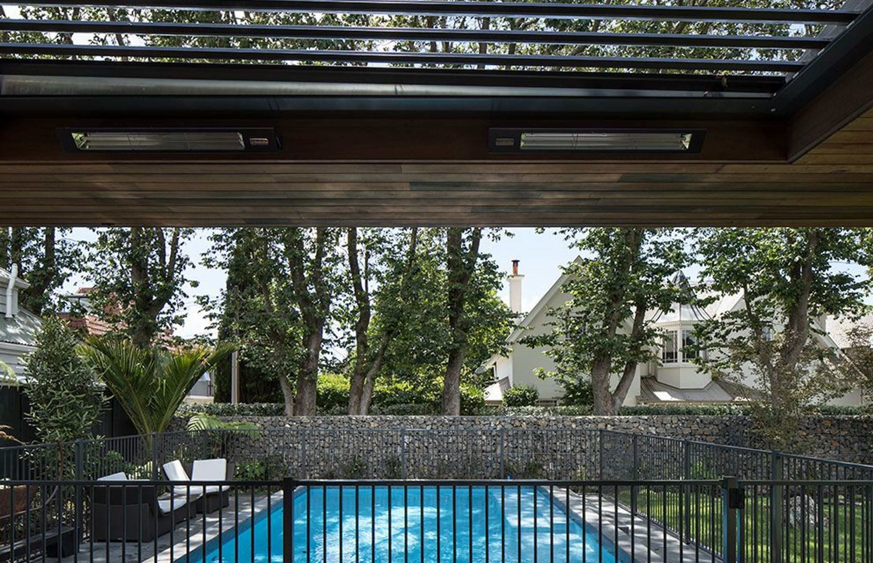An outdoor room overlooks the swimming pool, mature trees and a gubeon wall filled with volcanic rock excavated from the site prior to the build.