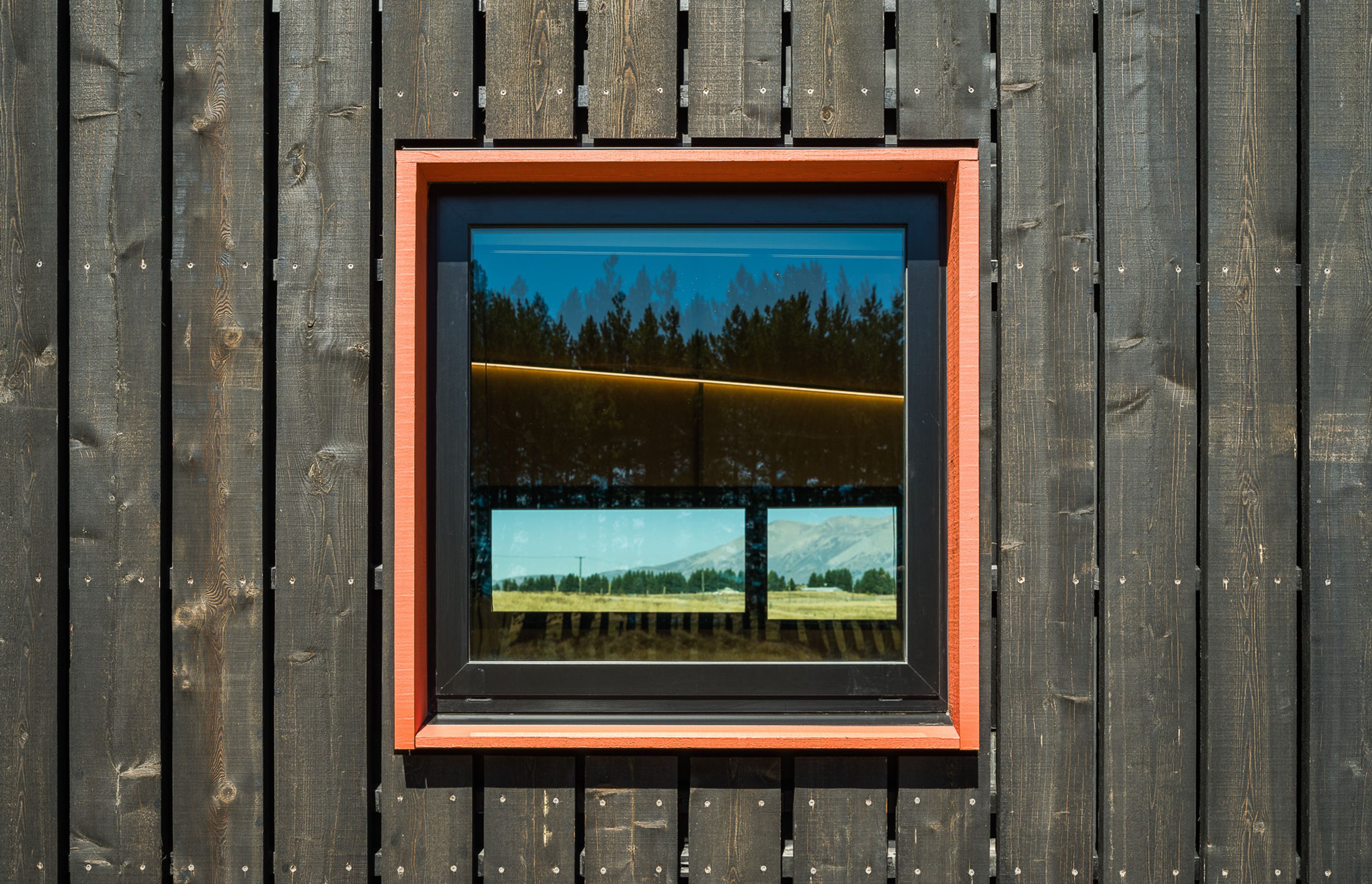 Burnt orange window frames punctuate the larch shell. The colour was a specific client request and has been used to emphasise the main structural elements.