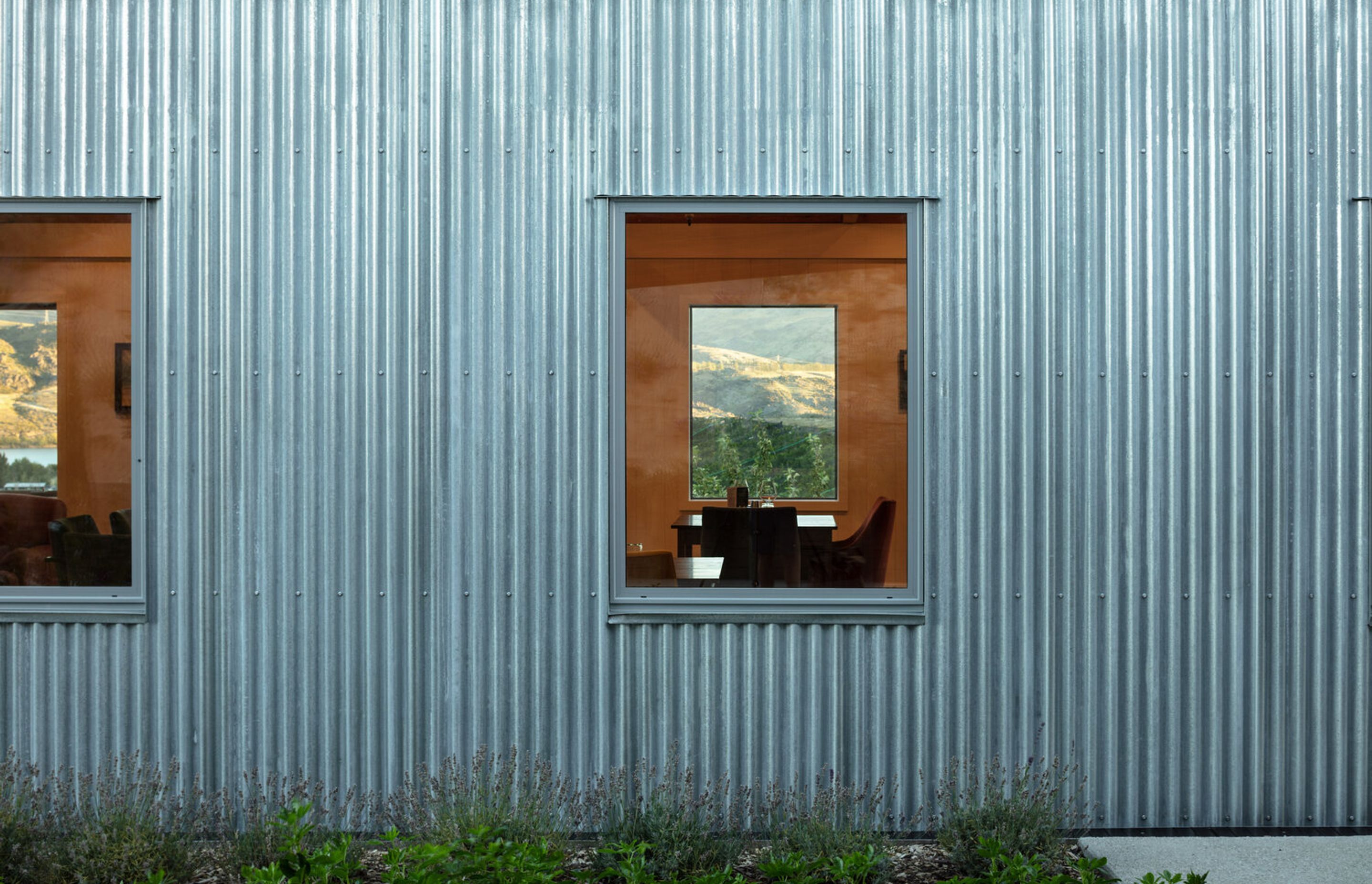 The simple geometry of picture windows allows glimpses right through the wine-tasting room to the view of the Clutha River and hills beyond.