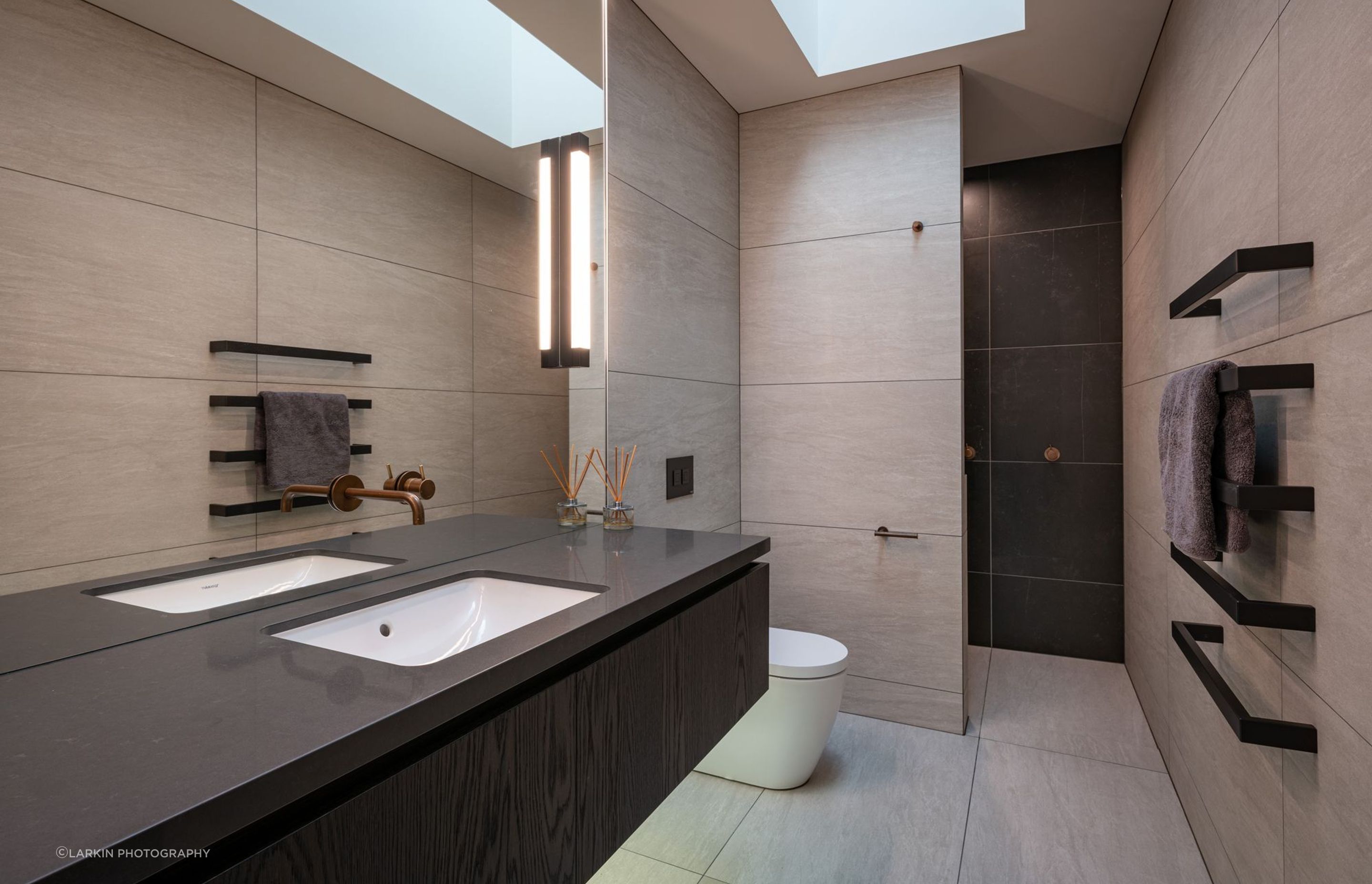 The family bathroom takes light in through a skylight and features dramatic monochromatic floor-to-ceiling tiles.