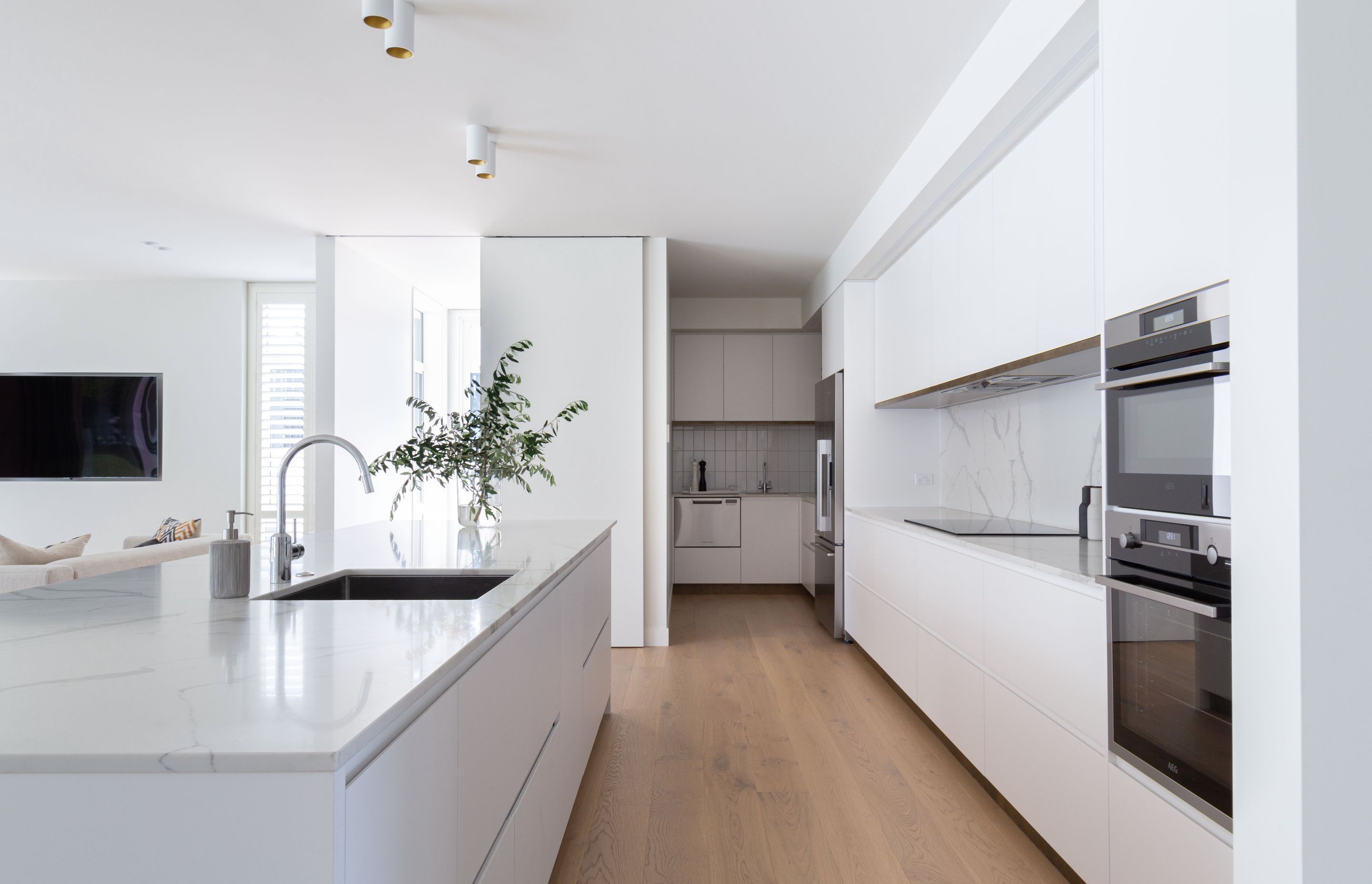 The kitchen's streamlined, white and marble materiality enhances the elegance and minimalism of the space.