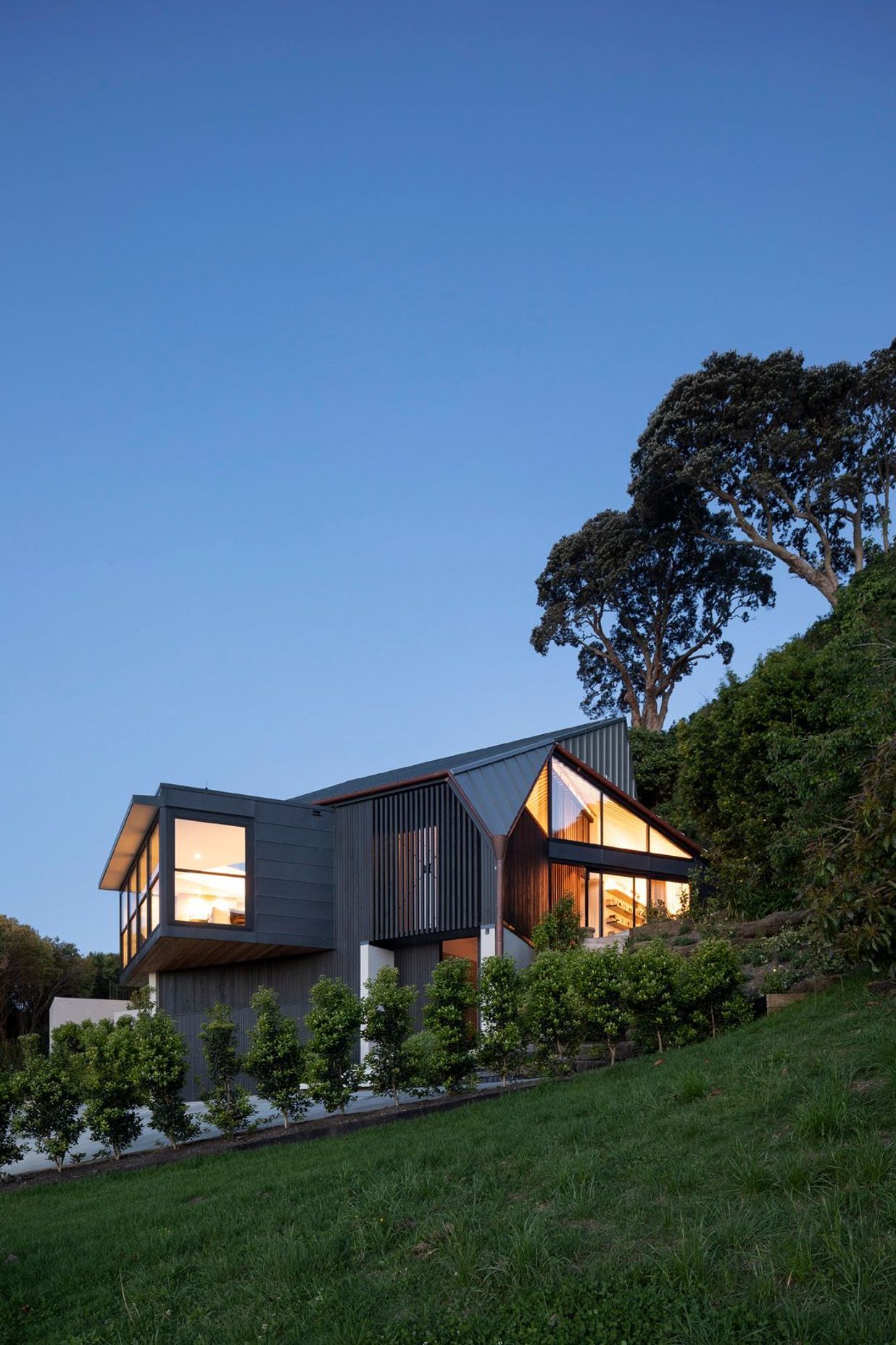 Situated at the end of a 500m driveway, which winds around 12 other houses, the home is perched on the slope of a volcanic crater with views over a wooded dell to the north and Auckland city to the west.